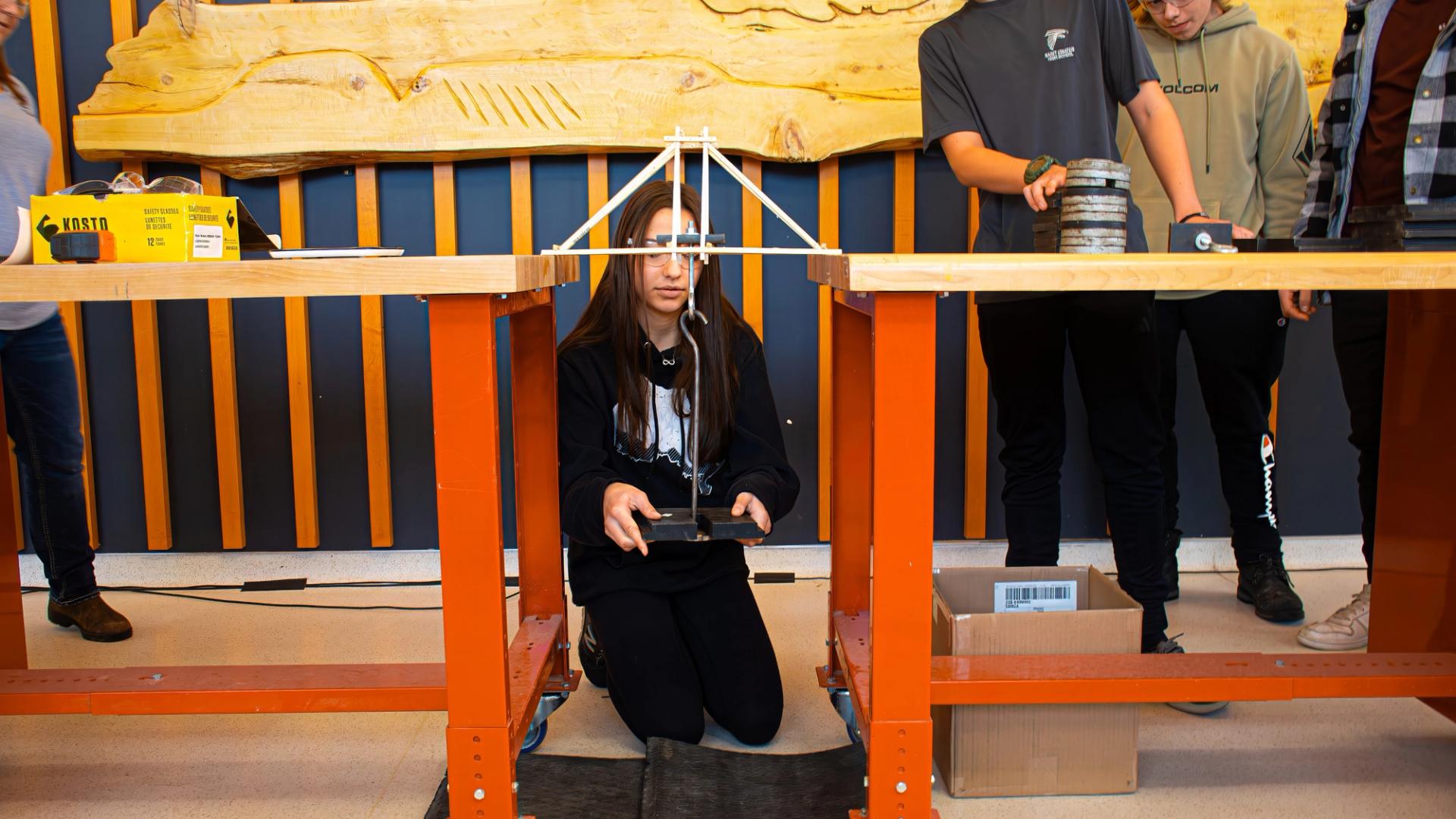 Students testing a model bridge with weights during a Confederation College engineering challenge
