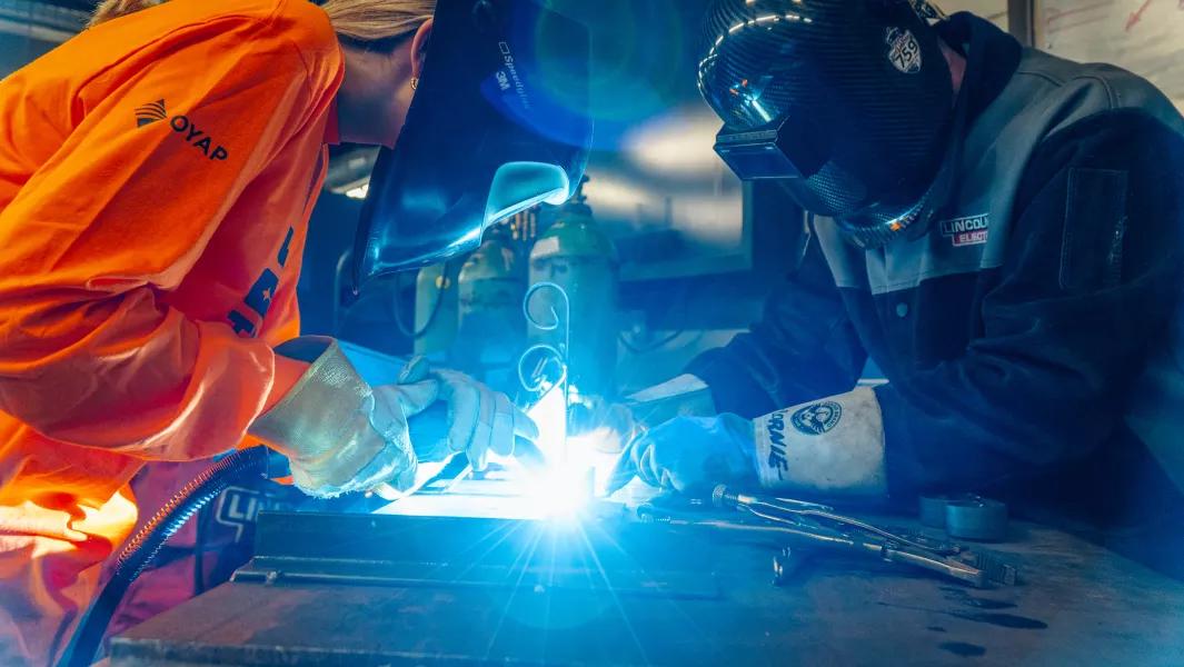 Two welders collaborating on a bright weld in a workshop