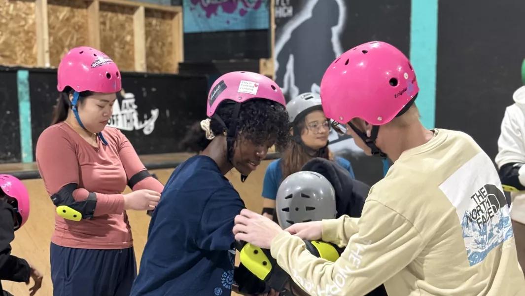 Students helping each other put on safety gear at an indoor skating venue