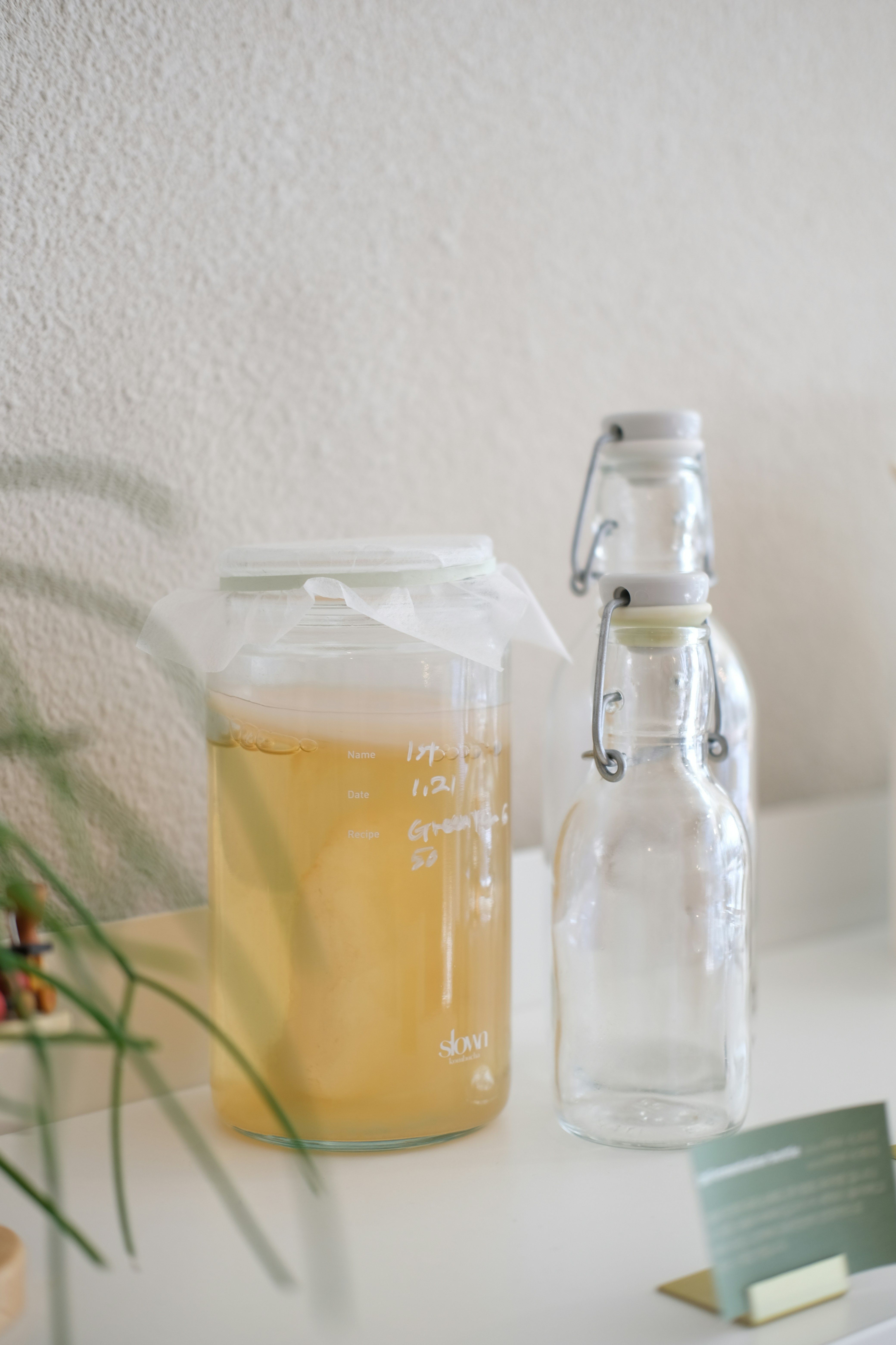 Glass jar covered with cloth and two empty swing-top bottles on a white surface