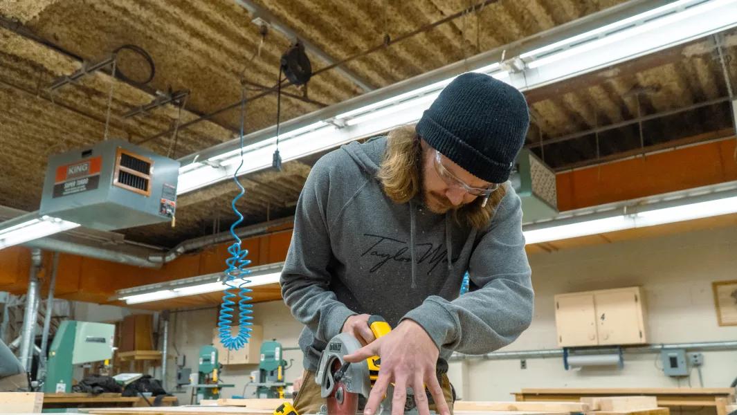 Student using a circular saw on a wood project in the carpentry shop