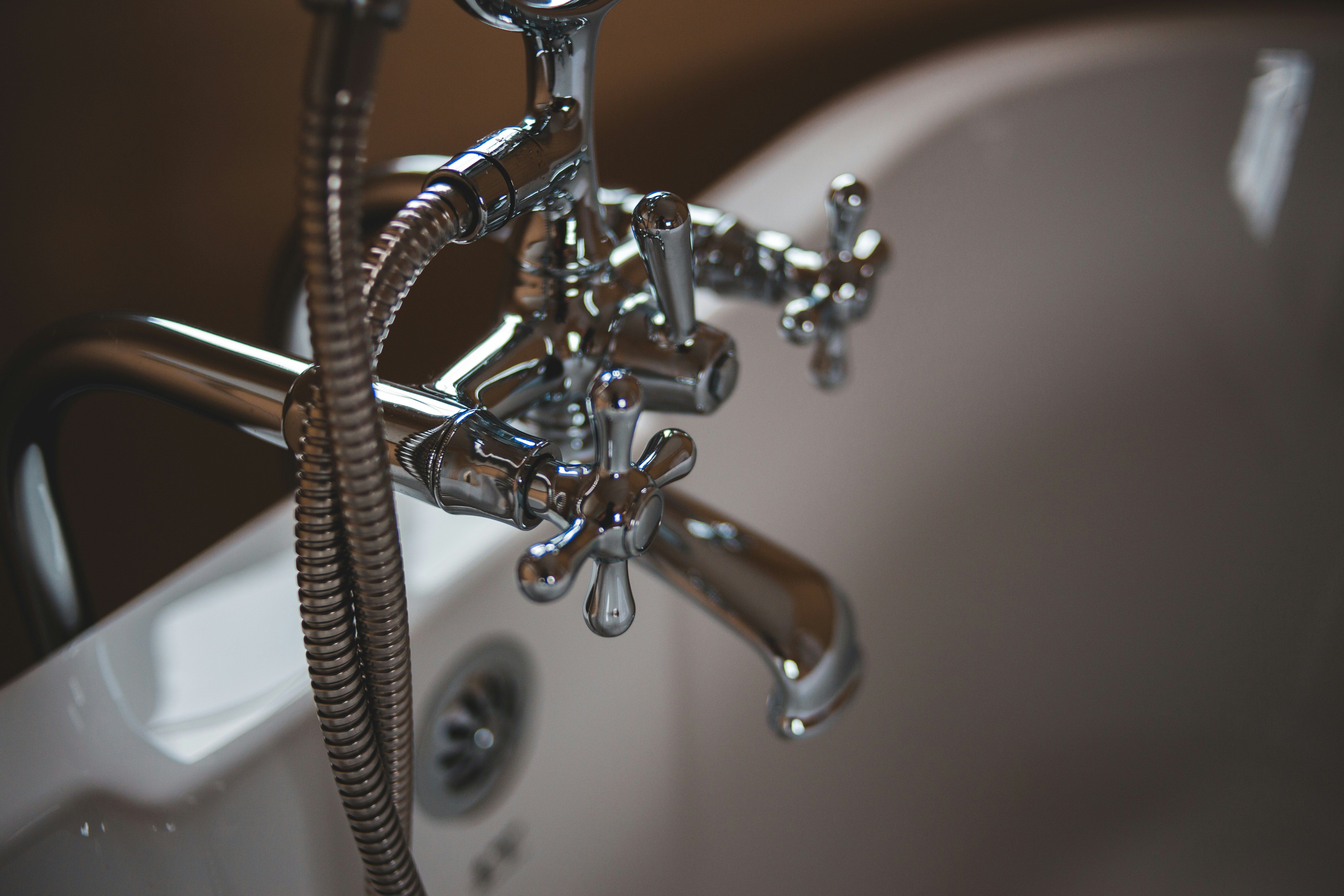 Chrome bath tap with cross handles beside a white sink and flexible shower hose