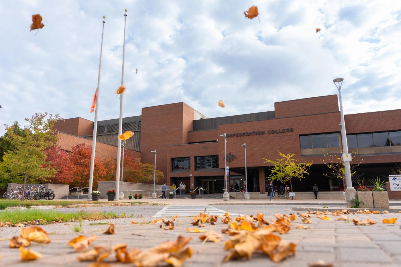 Confederation College campus entrance with students walking as autumn leaves fall in the foreground