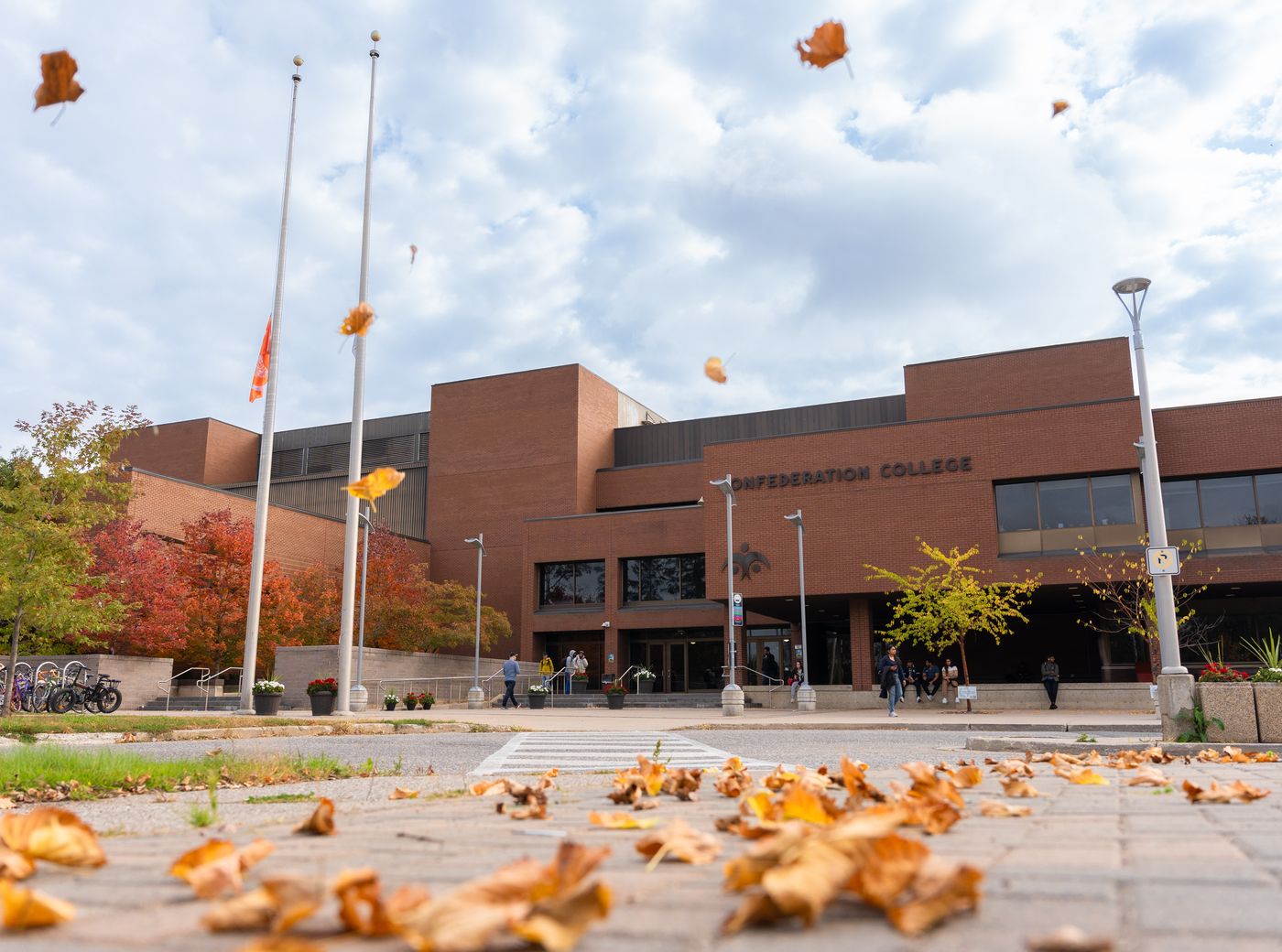Confederation College campus entrance with students walking as autumn leaves fall in the foreground