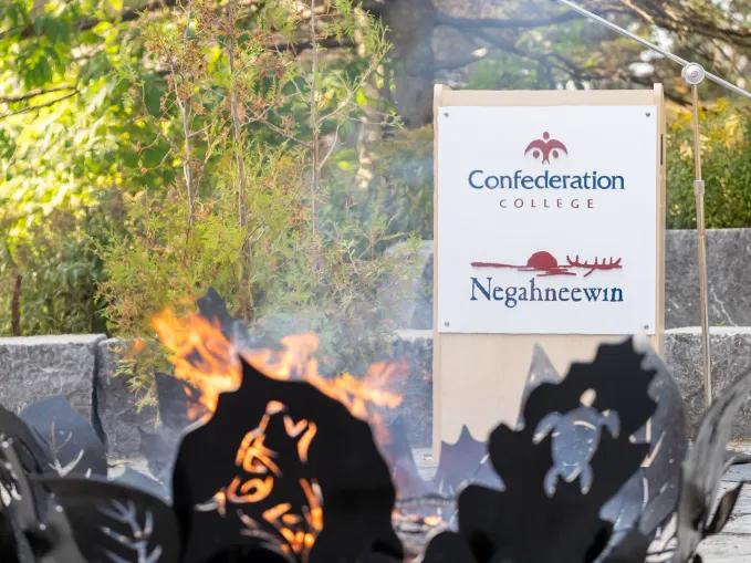 Confederation College Negahneewin sign behind a fire pit outdoors