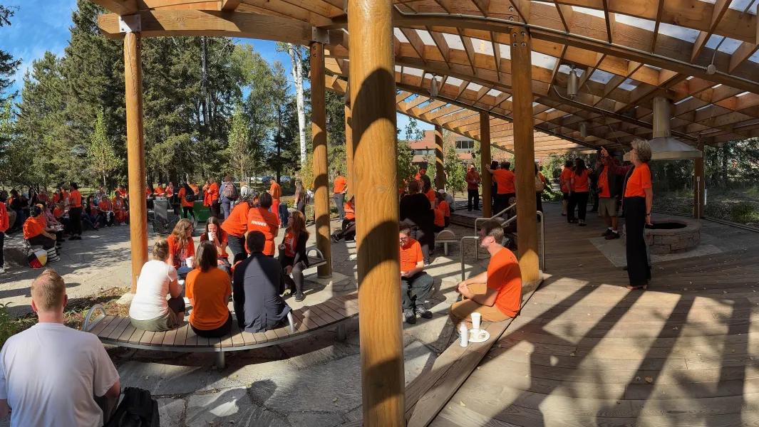 Large group wearing orange shirts gathered under a pavilion during a campus event