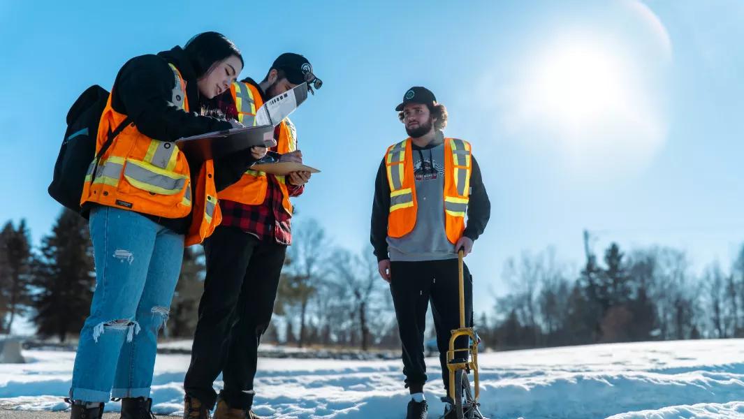 Students recording surveying measurements outdoors on a snowy field