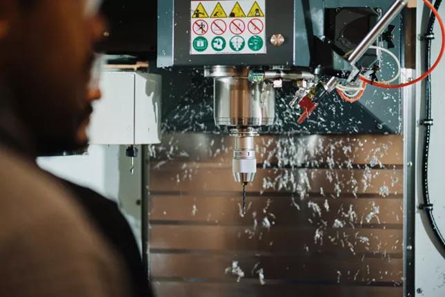 Worker operating a CNC machine with metal shavings flying during the machining process