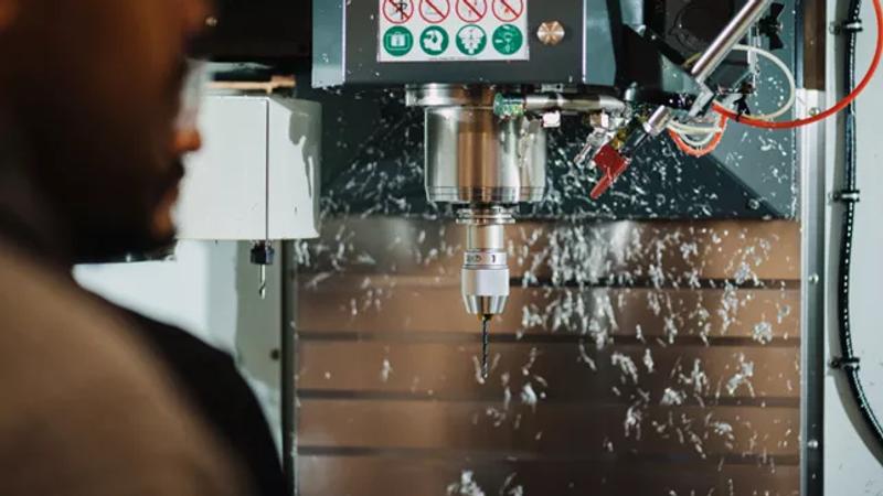 Worker operating a CNC machine with metal shavings flying during the machining process