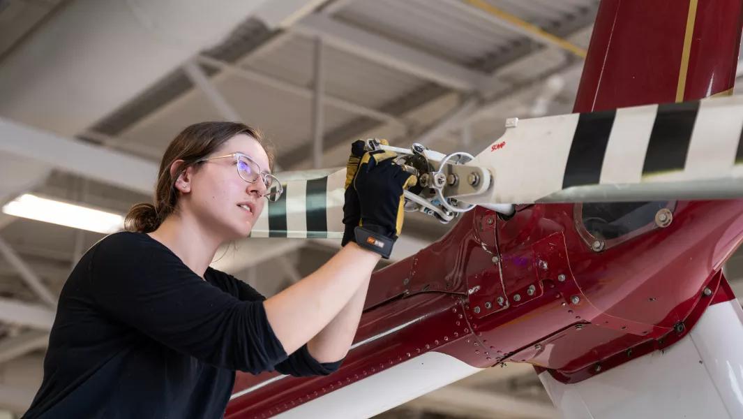 Student inspecting a helicopter rotor inside the aviation hangar