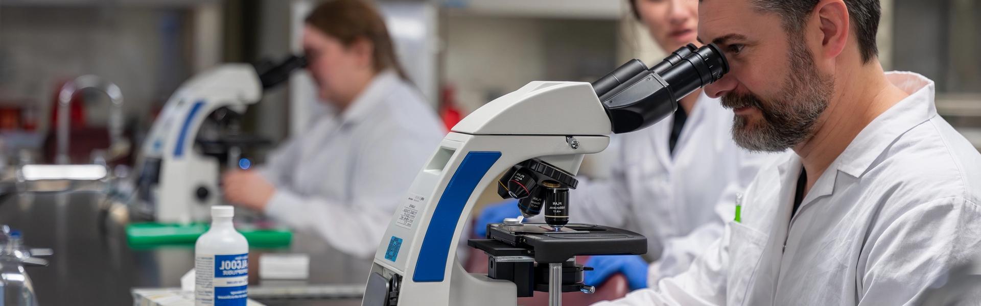 Students in lab coats examining samples with microscopes in a science laboratory