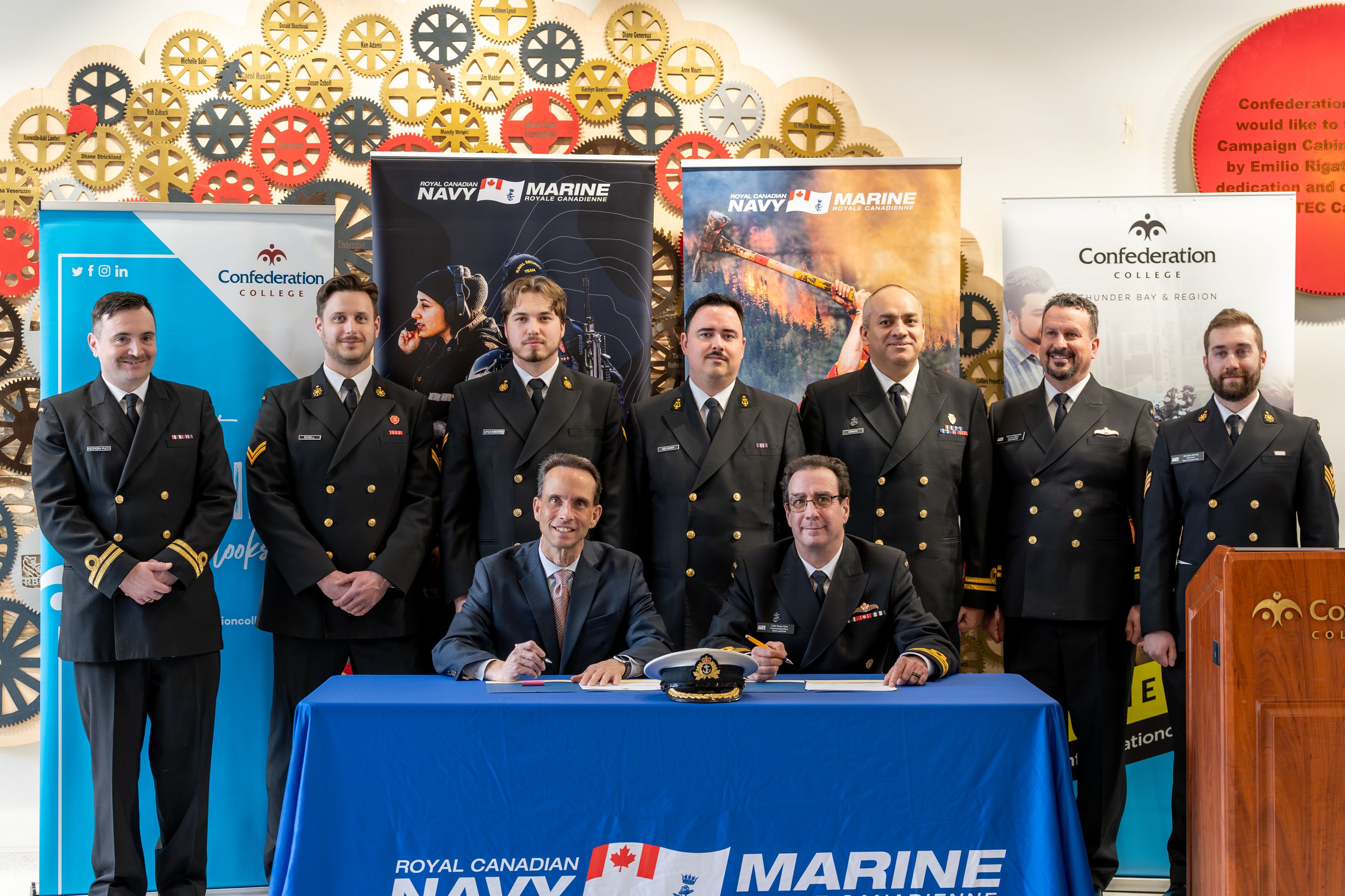 Royal Canadian Navy personnel and officials sign agreement at Confederation College with banners in background