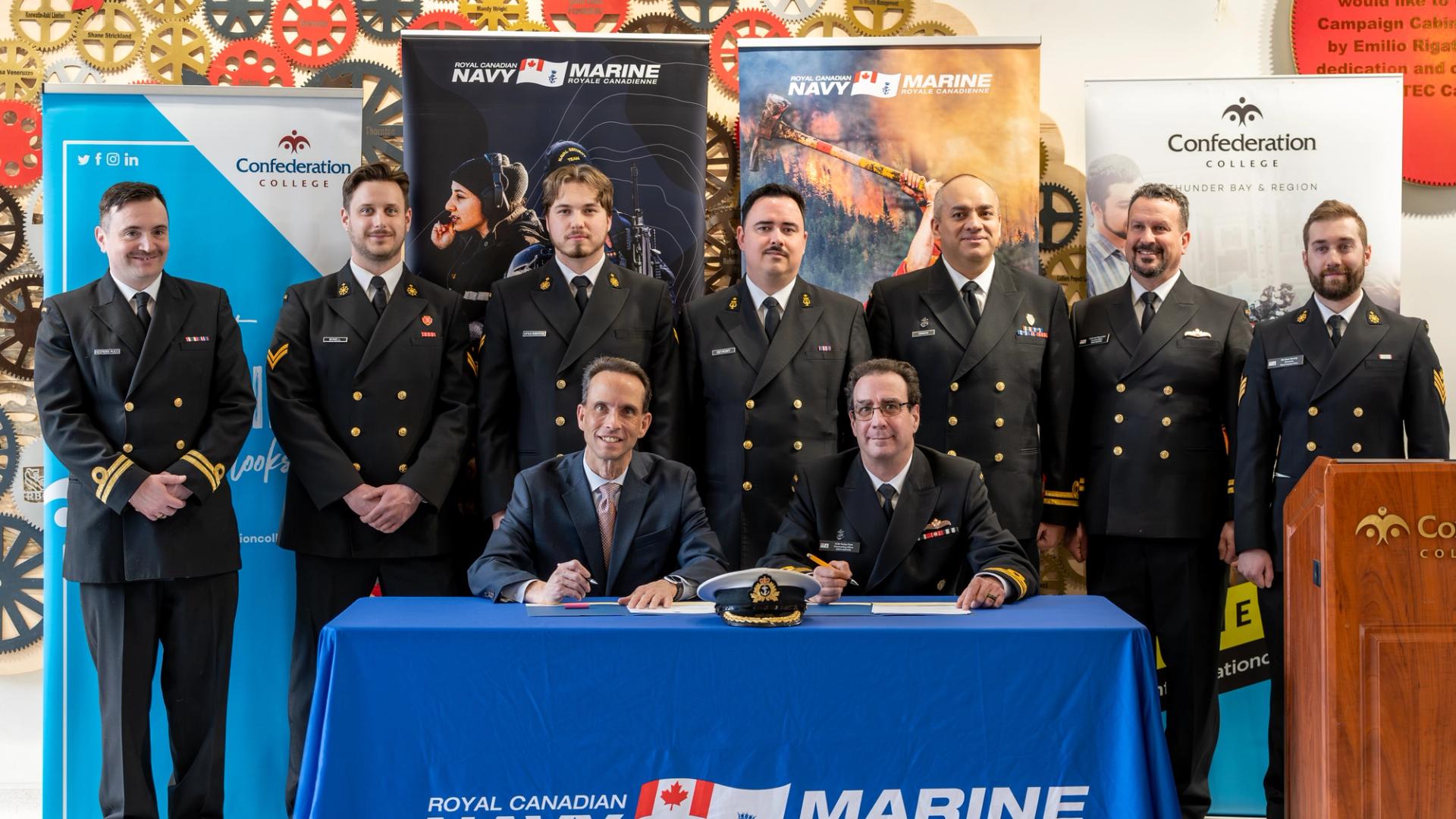 Royal Canadian Navy personnel and officials sign agreement at Confederation College with banners in background