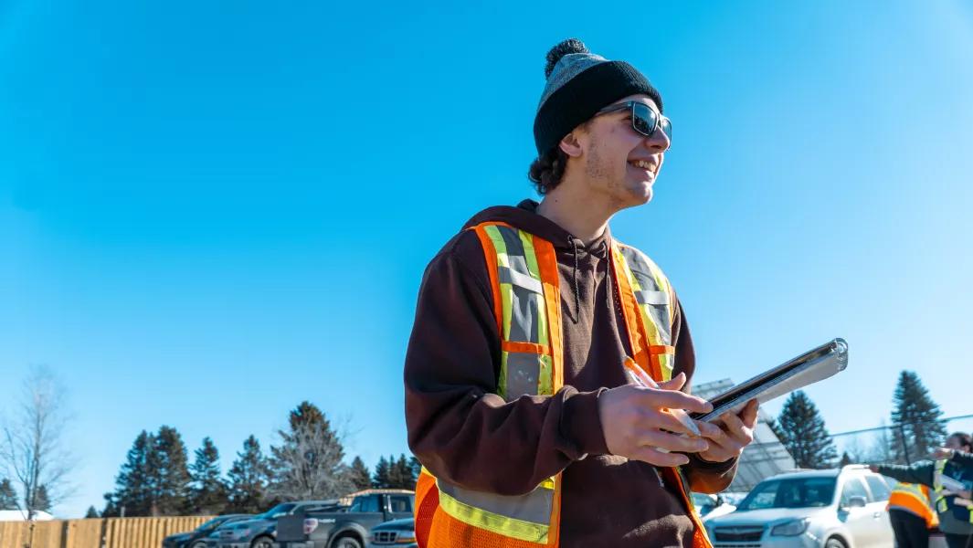 Student recording measurements outdoors while wearing a safety vest