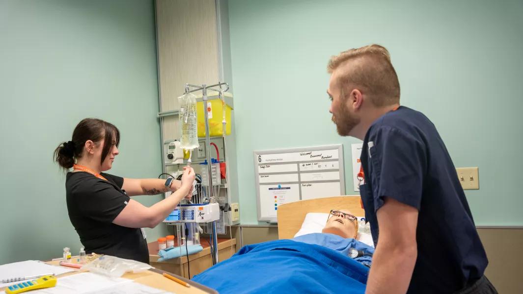 Nursing students setting up IV equipment beside a simulation mannequin