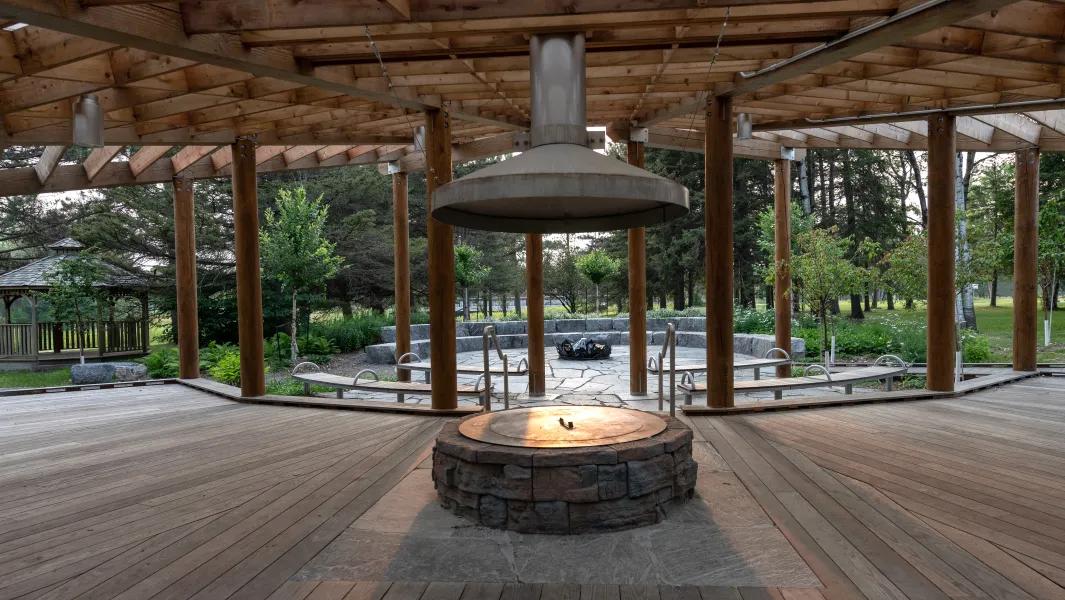 Open-air pavilion with central fire pit and seating during daytime
