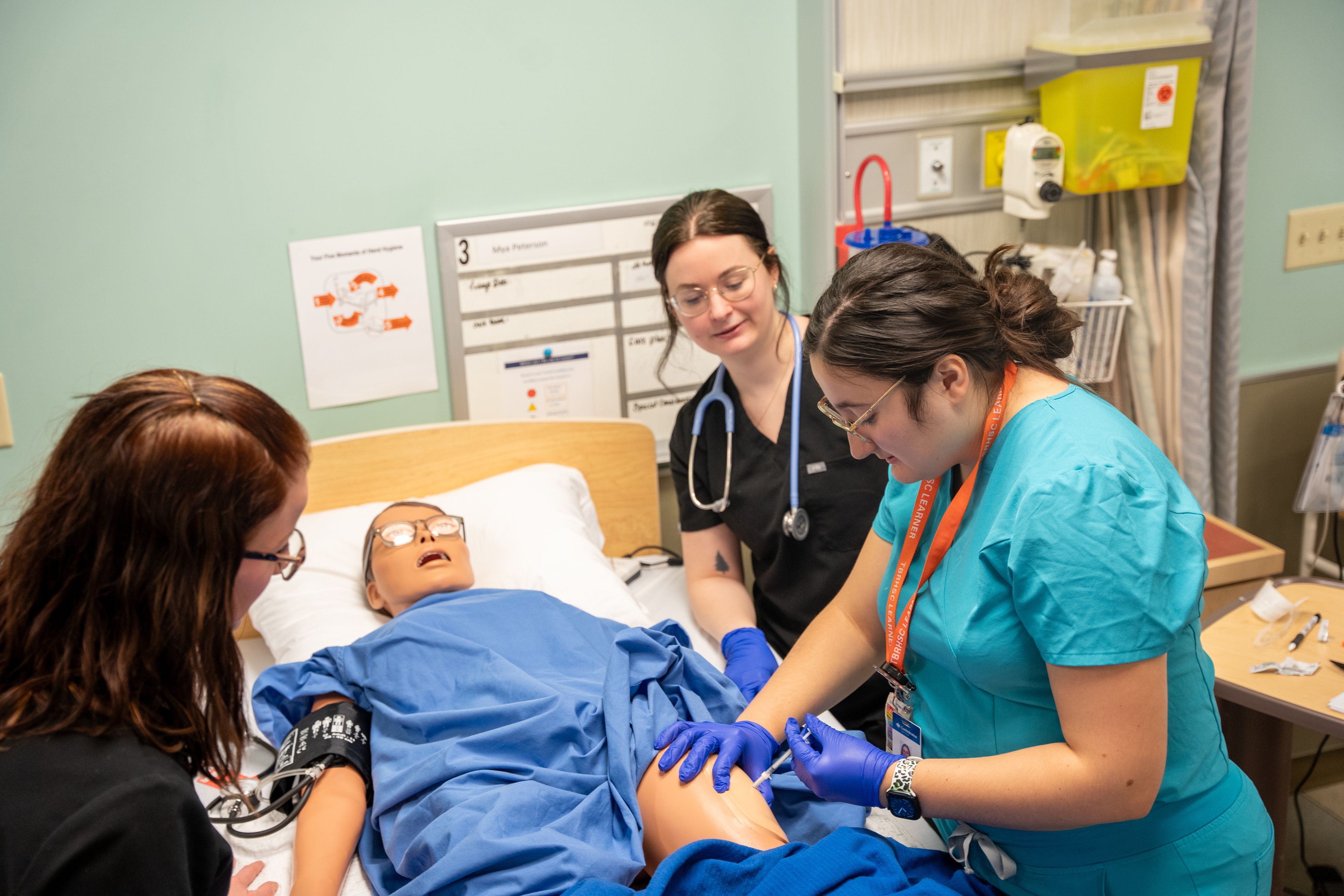 Nursing students practicing an injection on a medical simulation mannequin in a clinical lab setting