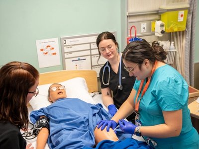 Nursing students practicing an injection on a medical simulation mannequin in a clinical lab setting