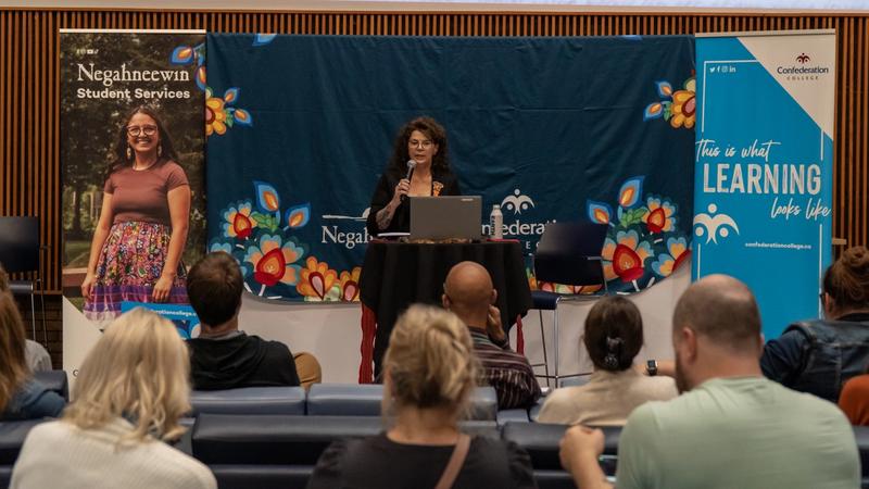 Speaker presents to an audience at a Negahneewin Student Services event with Confederation College banners.