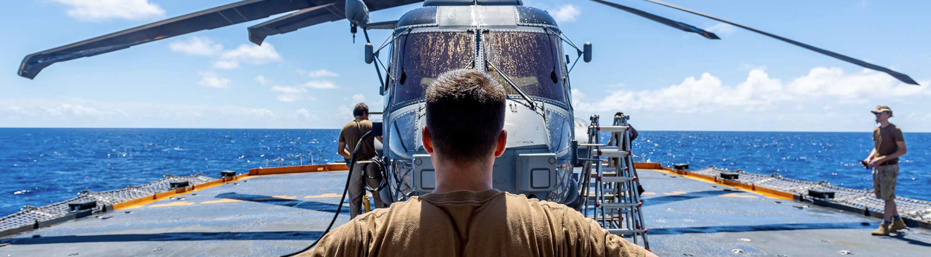 Student observing a helicopter on a ship deck during marine and aviation training at sea