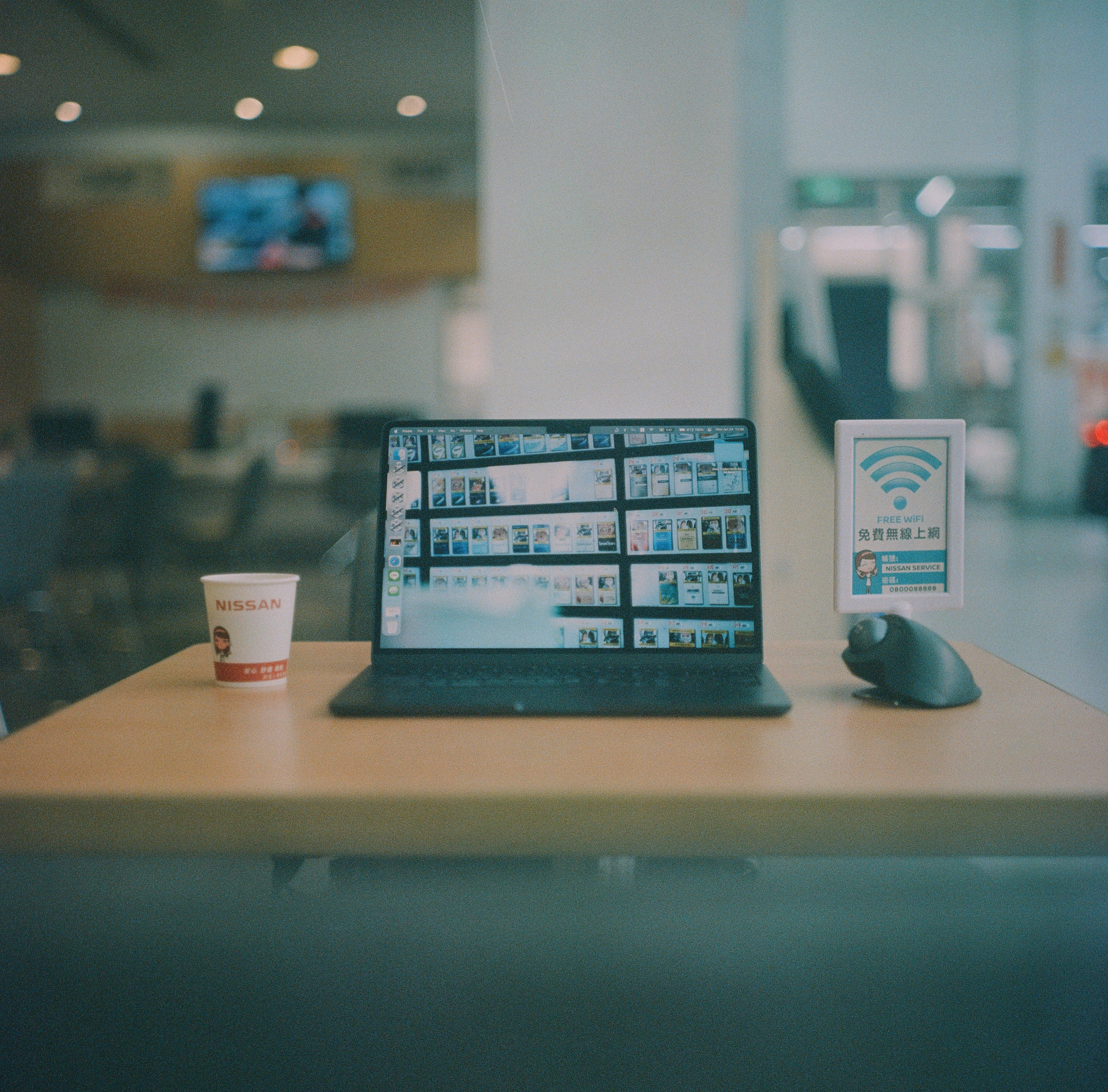 Laptop workstation displaying digital media projects beside a free Wi-Fi sign in a public space