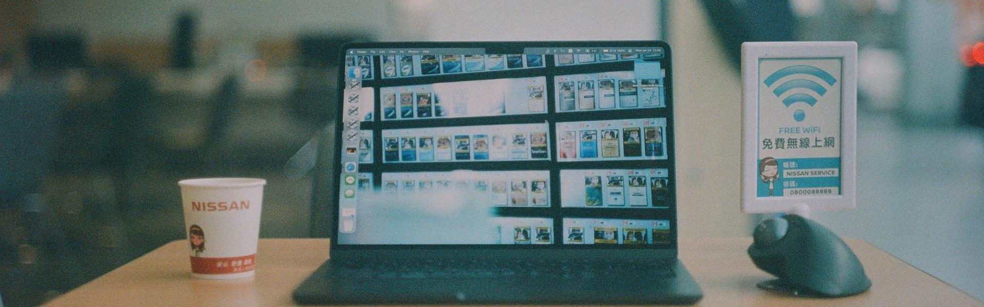 Laptop workstation displaying digital media projects beside a free Wi-Fi sign in a public space
