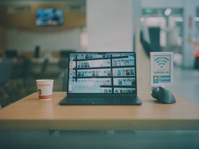 Laptop workstation displaying digital media projects beside a free Wi-Fi sign in a public space