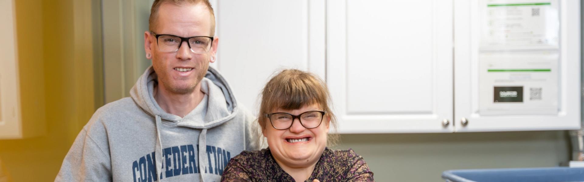 Two people standing in a laundry room, one in a Confederation College hoodie and the other giving a thumbs-up.