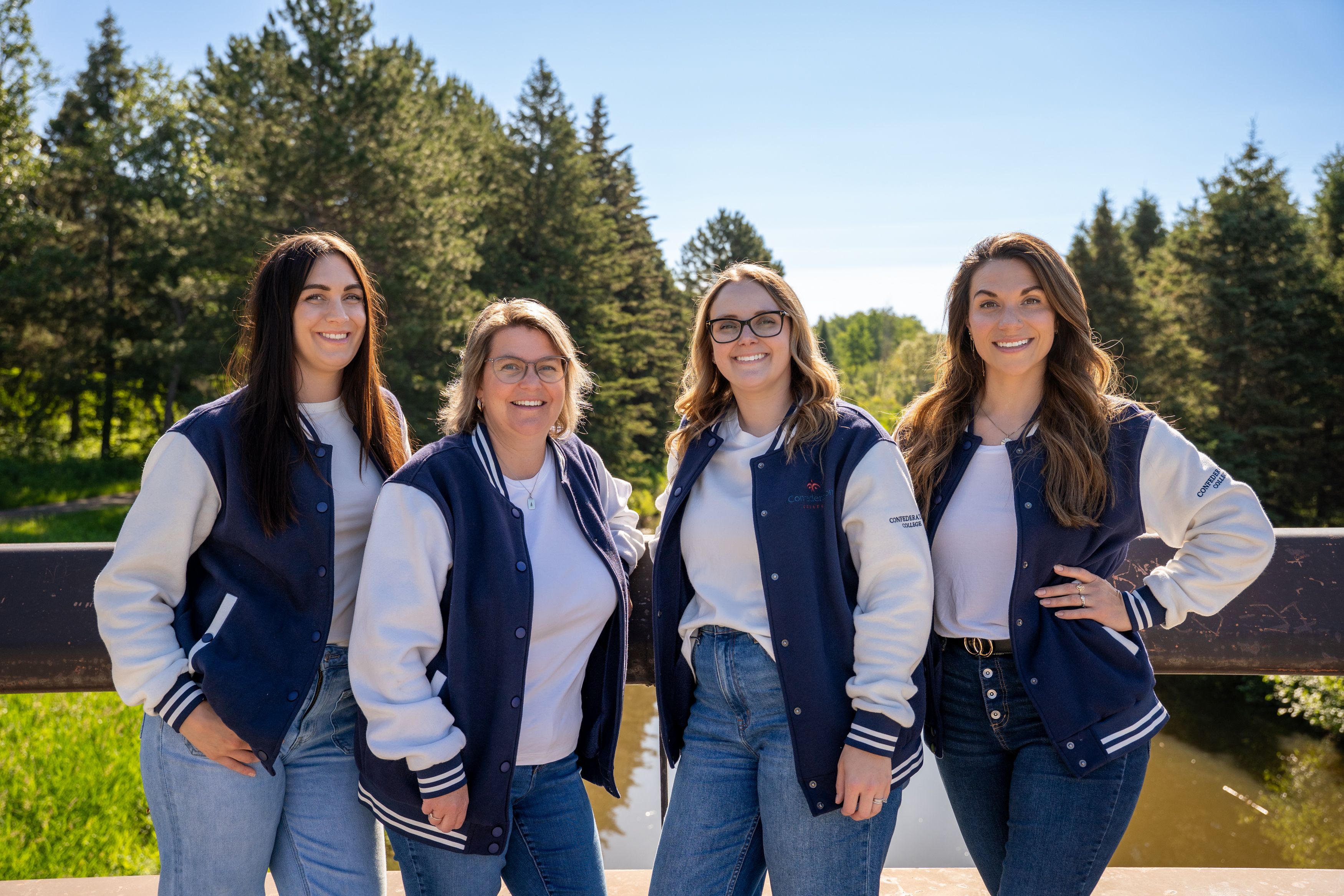 Four women standing outdoors in matching navy-and-white varsity jackets