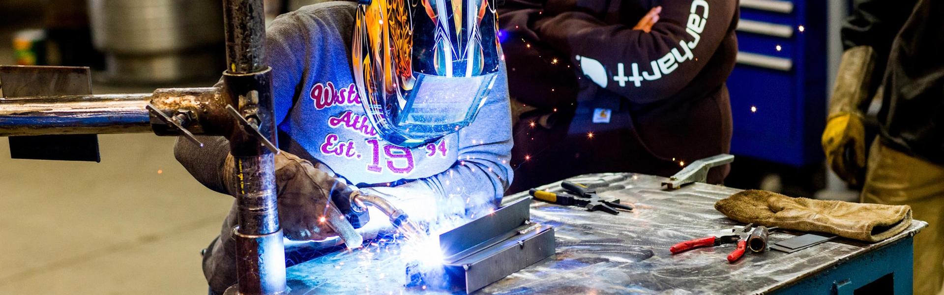 Welding apprentices practicing metal welding with protective helmets in a shop