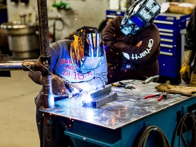 Welding apprentices practicing metal welding with protective helmets in a shop