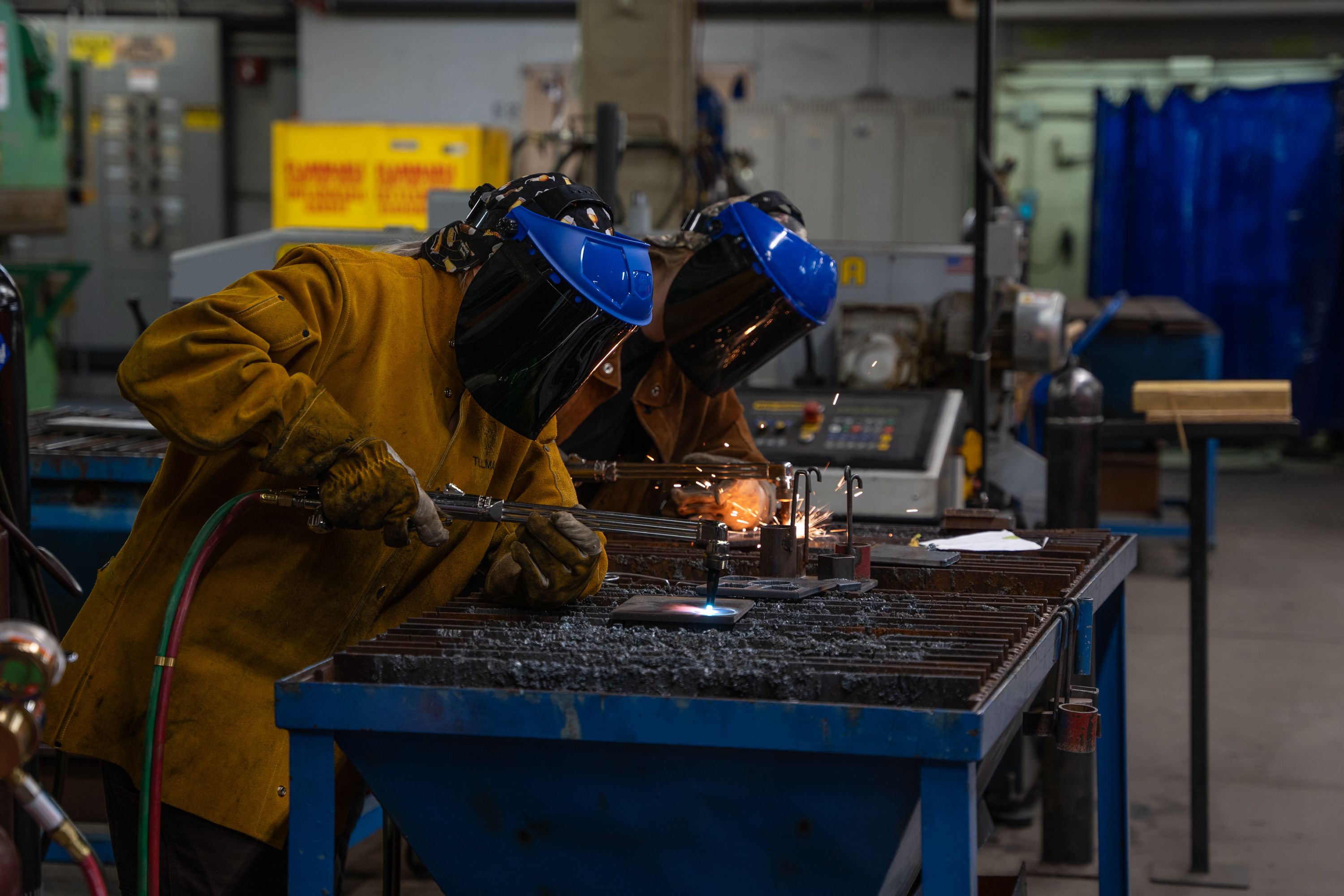 Students using oxy-fuel torches to cut metal in a welding lab while wearing protective safety gear
