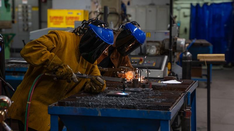 Students using oxy-fuel torches to cut metal in a welding lab while wearing protective safety gear