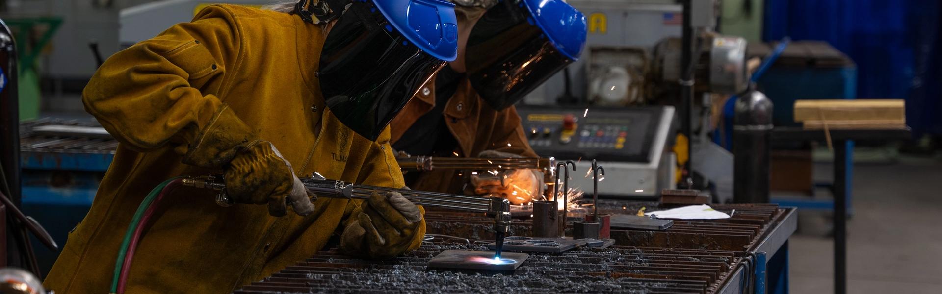 Students using oxy-fuel torches to cut metal in a welding lab while wearing protective safety gear