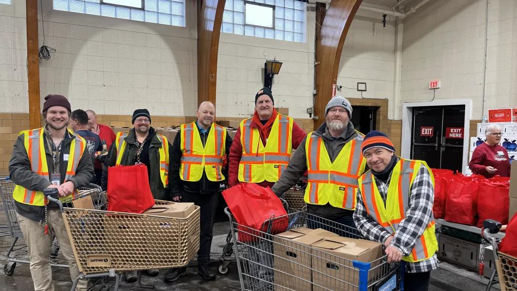 Volunteers in safety vests stand with carts of donated goods inside a community hall