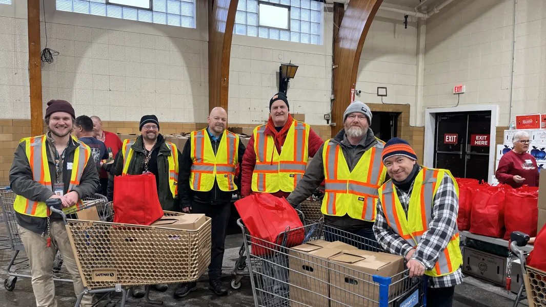 Volunteers in safety vests stand with carts of donated goods inside a community hall