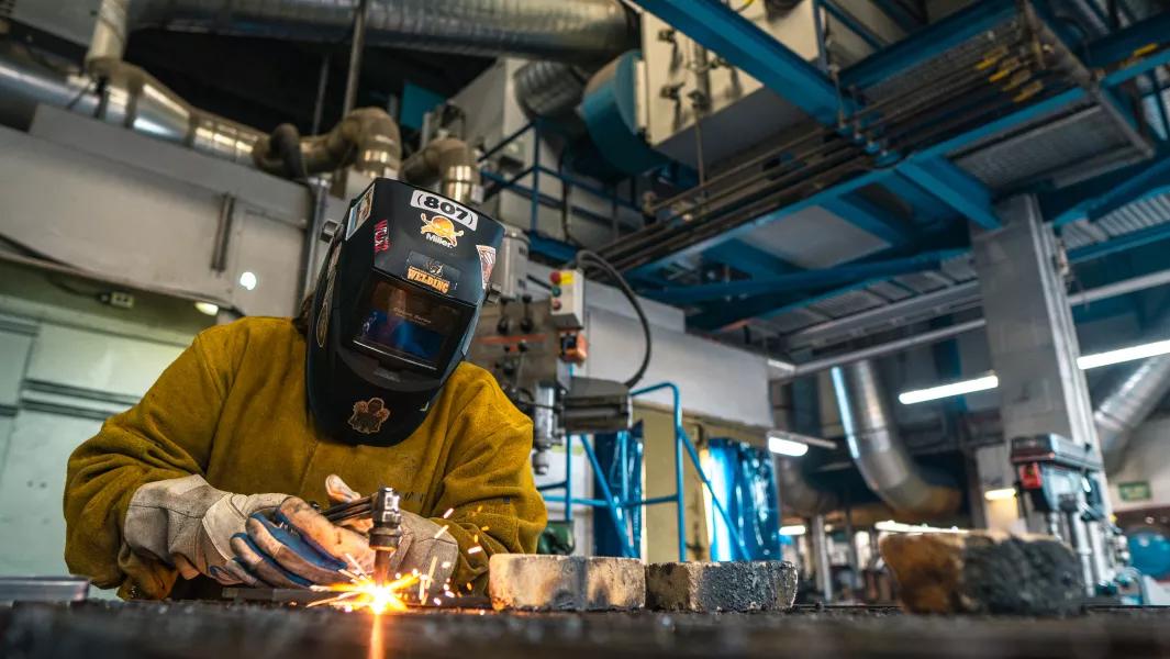 Welder cutting metal on a workbench in an industrial shop with sparks flying