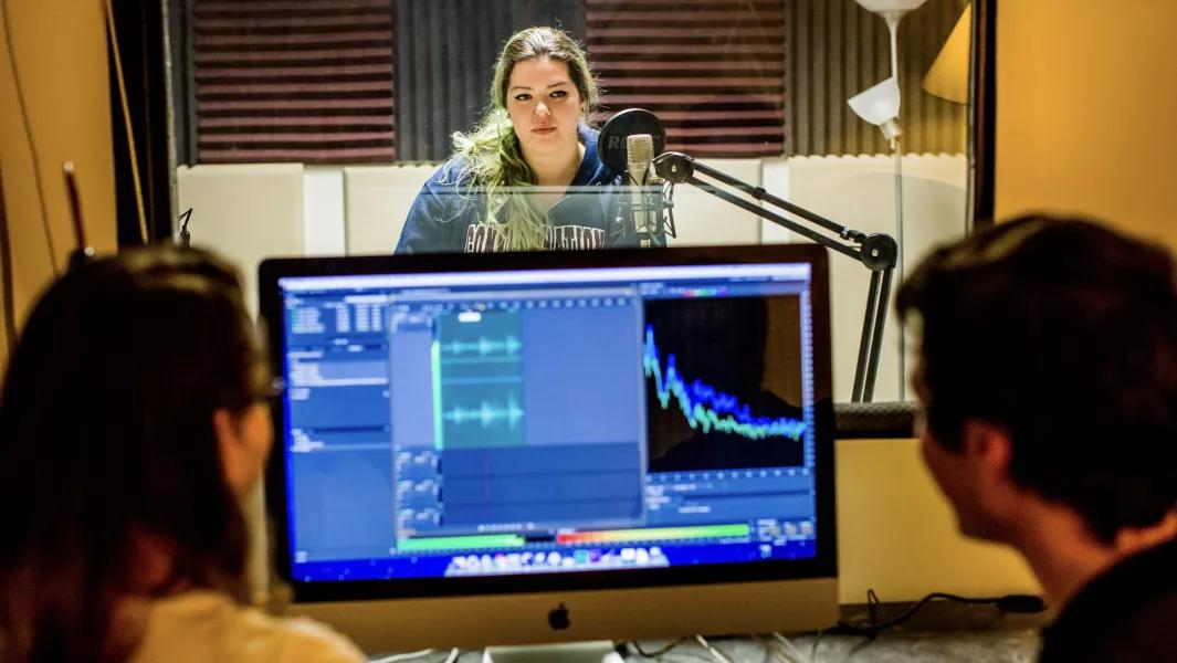 Student recording vocals while classmates monitor audio levels