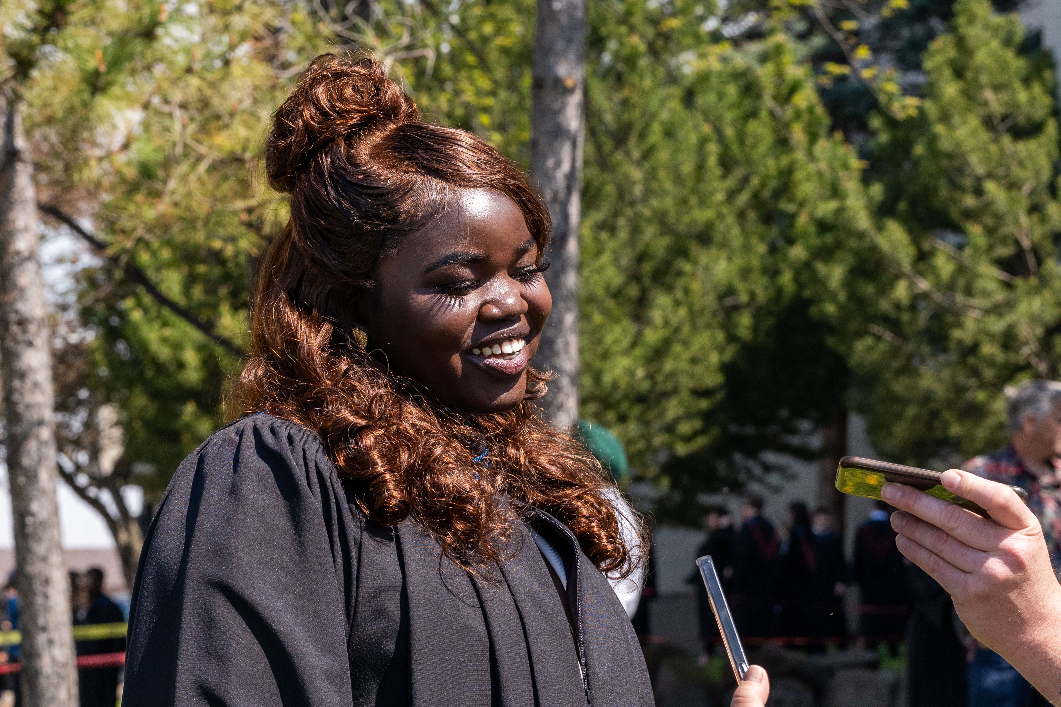 Graduate in convocation gown speaks with media outdoors after a Confederation College ceremony