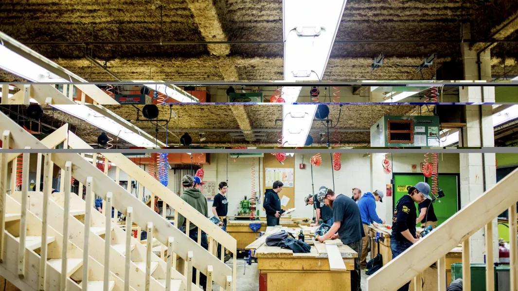 Wide view of carpentry students working at benches in a large woodworking shop