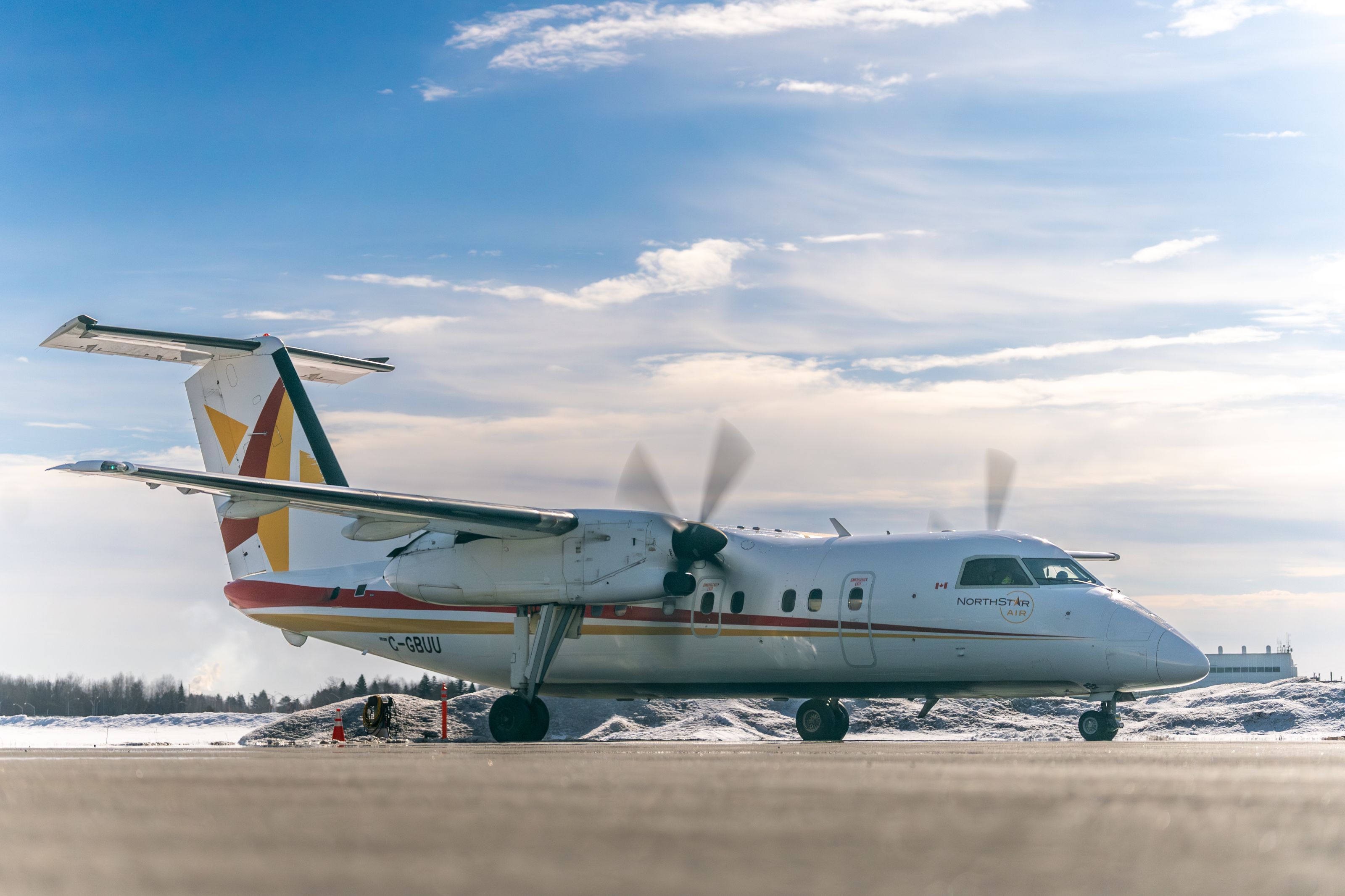 A white North Star Air turboprop airplane sits on a snowy runway under a bright sky. The aircraft is shown in profile with its propellers blurred from motion and colored stripes on the tail and fuselage