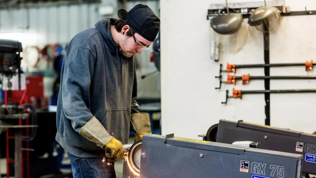 Student grinding metal using shop equipment while wearing safety gear