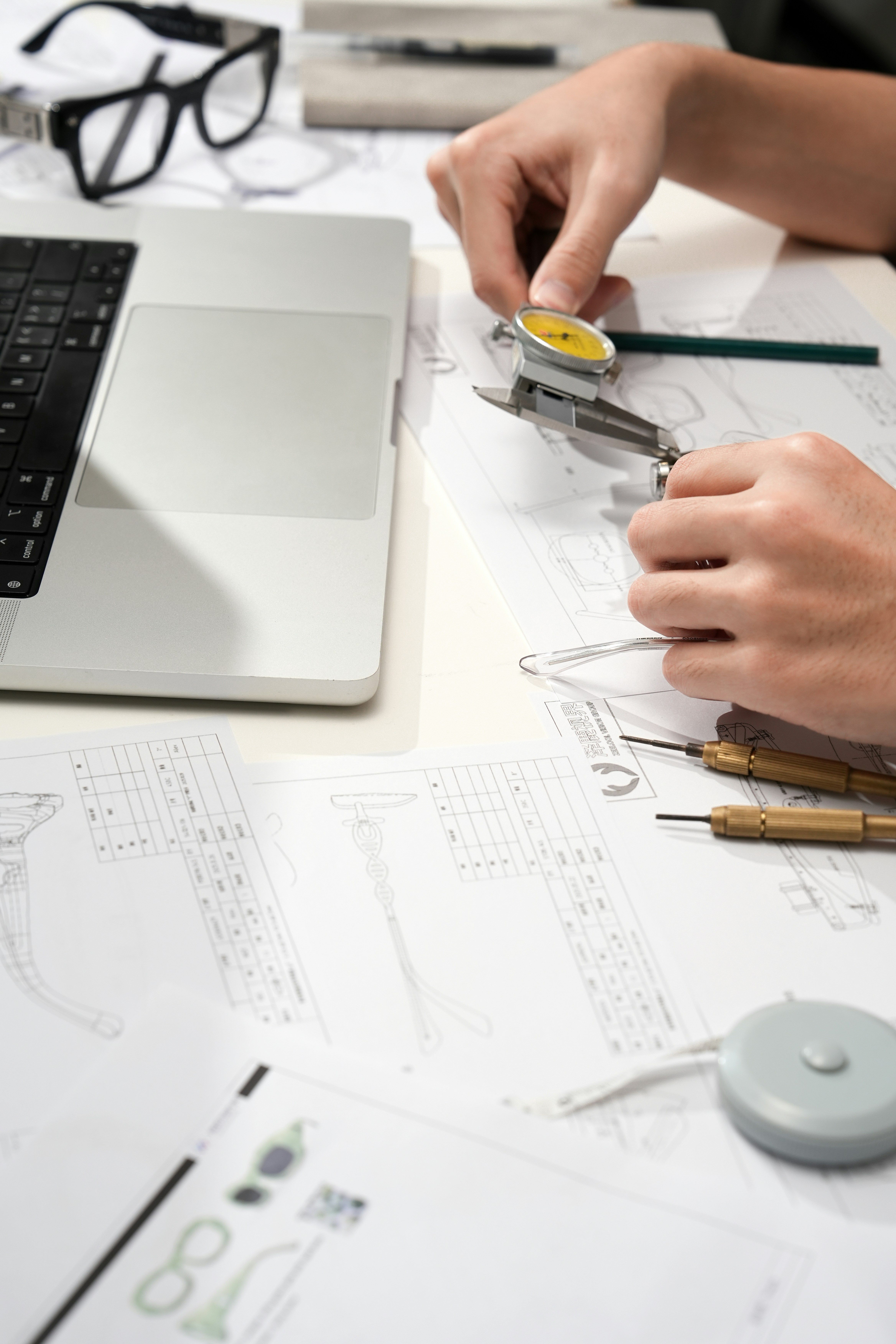 Student using precision measuring tools to review technical design drawings at a workstation