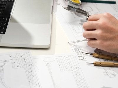 Student using precision measuring tools to review technical design drawings at a workstation