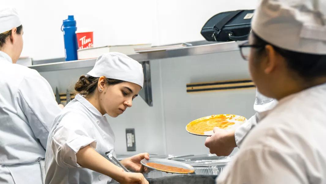 Culinary students plating sauces and dishes together in a commercial kitchen classroom