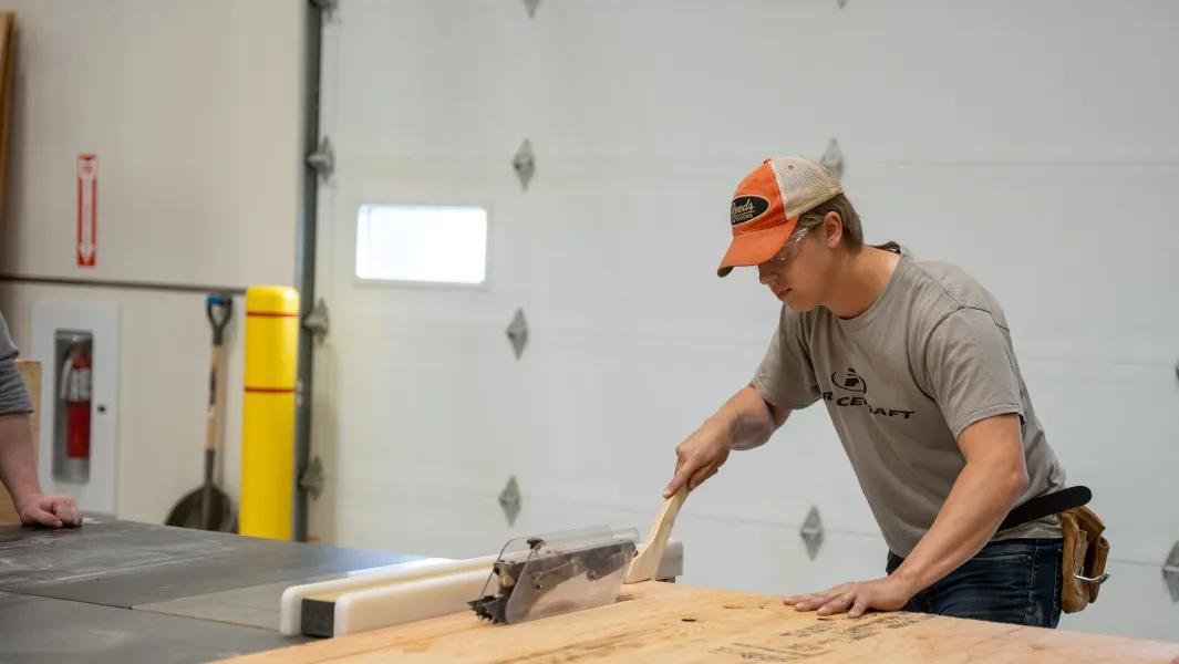 Student cutting plywood on a table saw in the carpentry shop