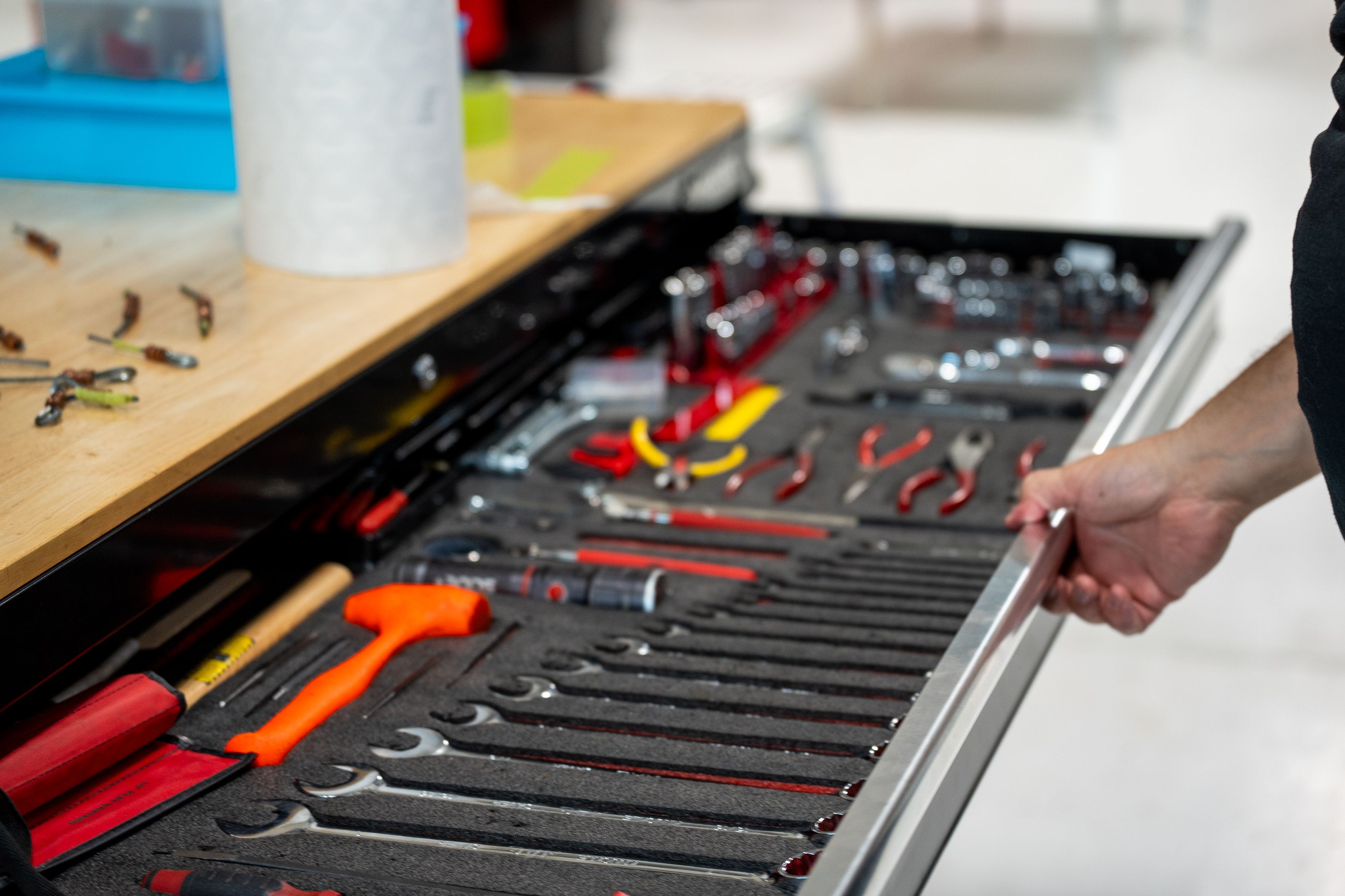 A hand pulls open a tool chest drawer holding neatly arranged wrenches, pliers, screwdrivers and other tools.