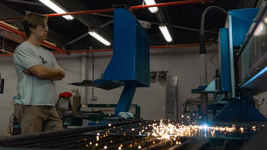 Student monitoring a CNC cutting machine as it produces sparks