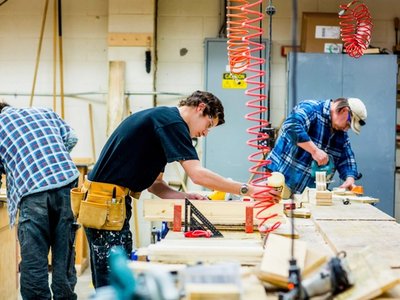 Roofer apprentices measuring and cutting lumber in a training workshop