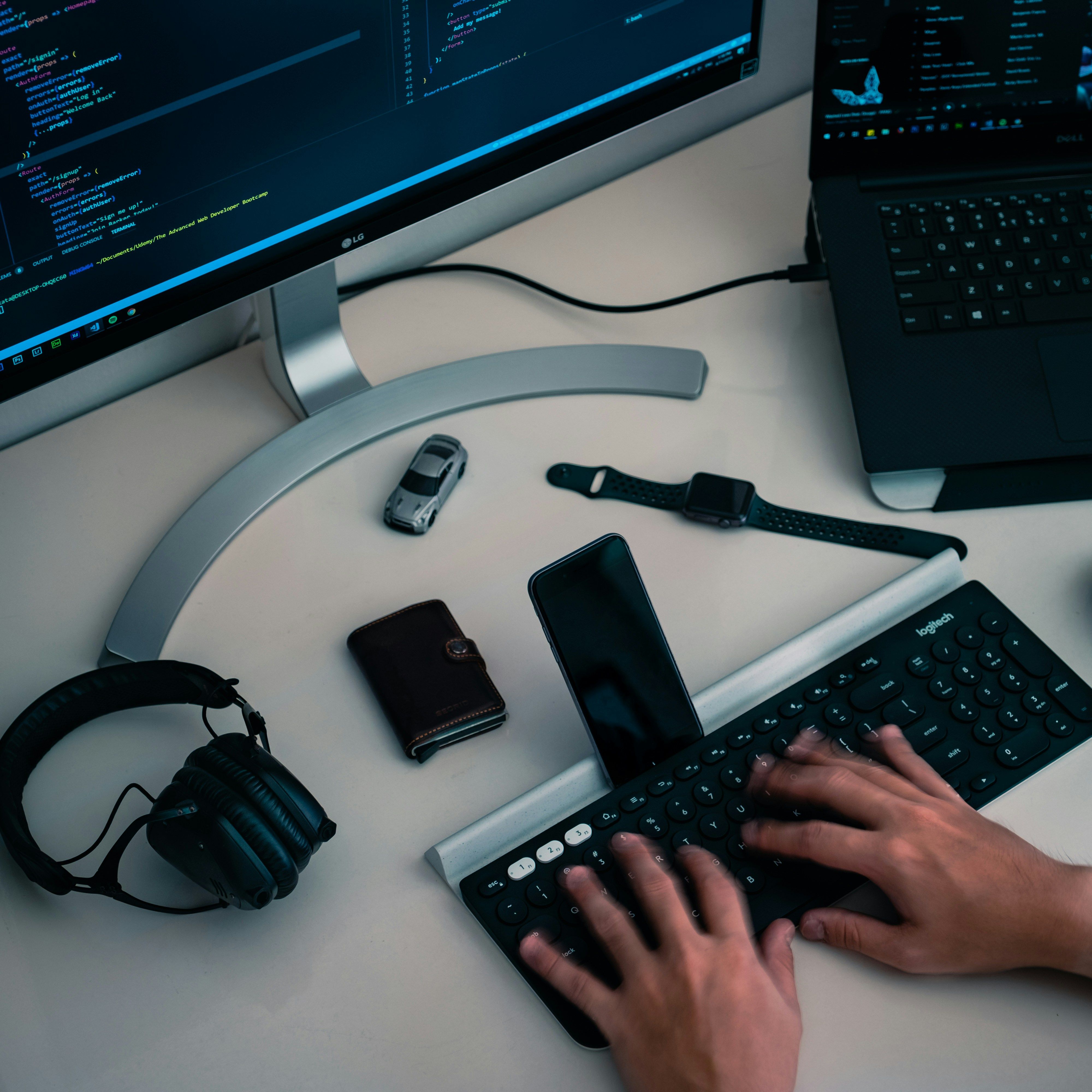 Student coding at a workstation with multiple devices, including a monitor, laptop, and smartphone